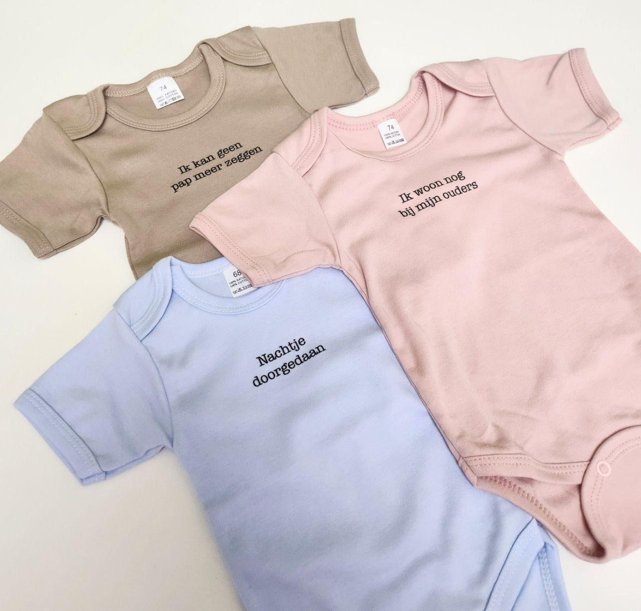 Trio van drie body's in het beige, roze en blauw. Op de body's staan grappige teksten. Het zijn leuke babycadeaus